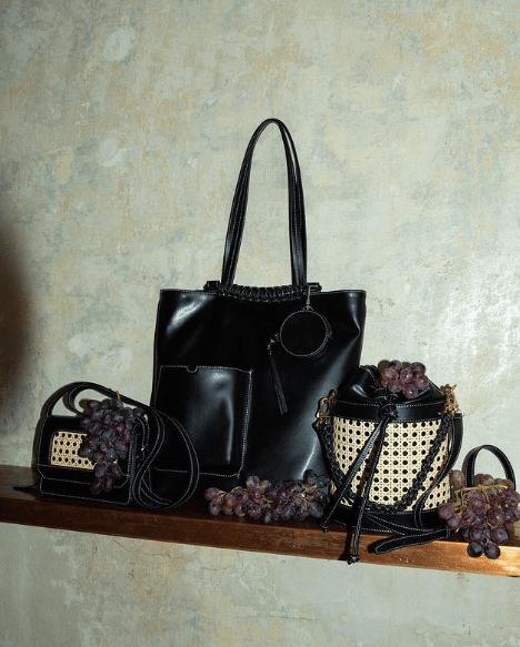 A black grape leather handbag with two smaller bags beside them decorated with grapes