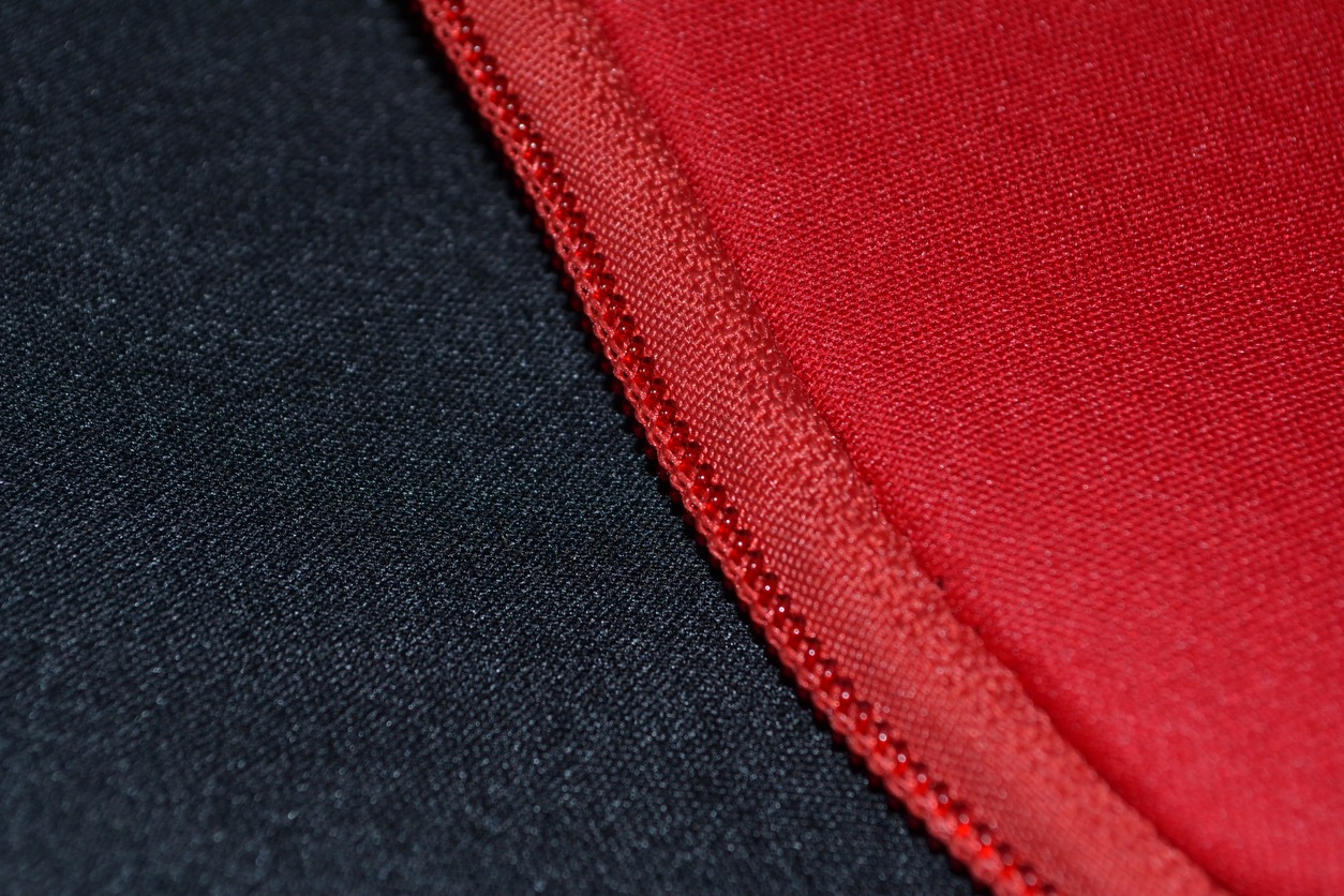 A close-up of a zipper attached to the materials of red and black neoprene.