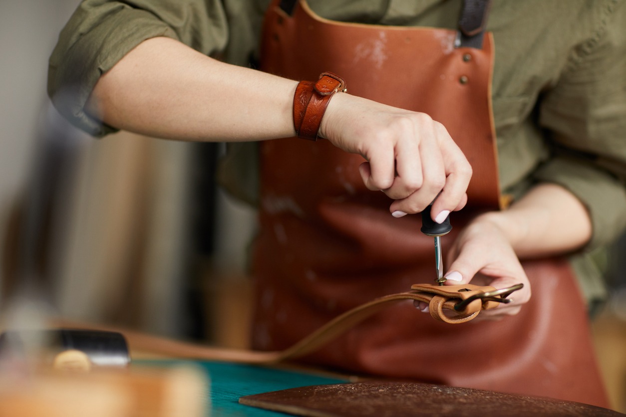 A female artisan making leather belt in leatherworking shop