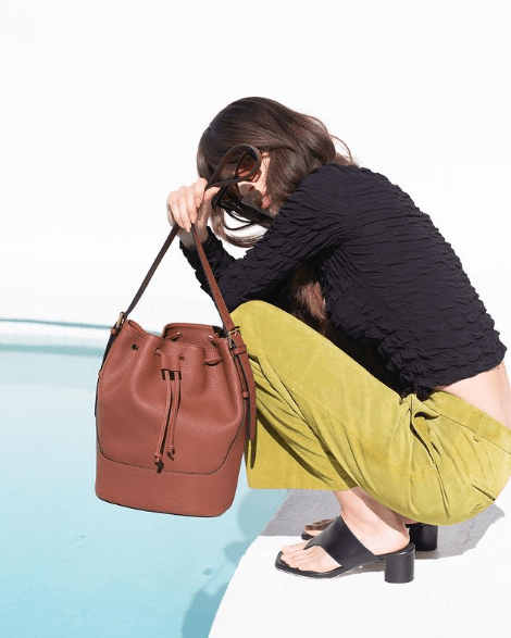 A woman sitting and holding a brown upcycled leather bucket bag