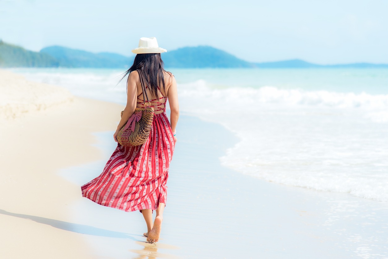 A woman wearing a dress by the beach and wearing a woven beach bag