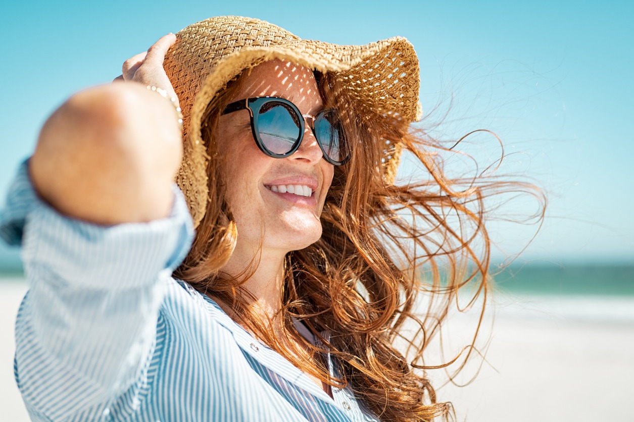 Beautiful woman enjoying the beach from the side wearing sunglasses.