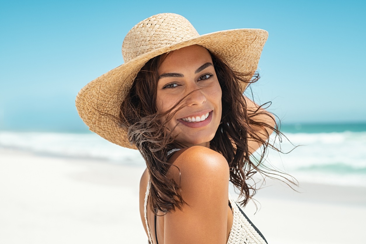 Beautiful young woman wearing a straw hat in a beachfront portrait with the ocean in the background.