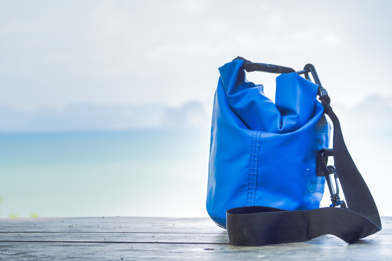 Blue water-resistant bag on wooden table with indistinct background seascape.