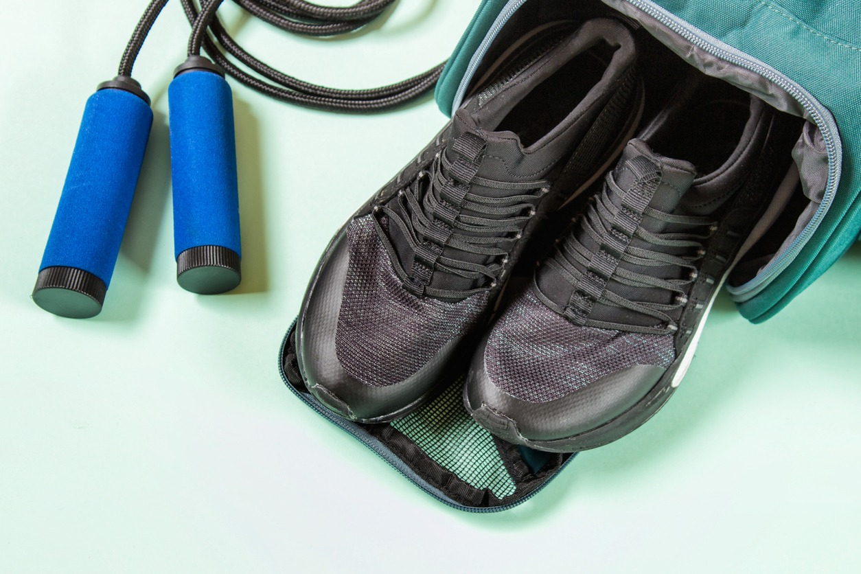 Jump rope handles and sports shoes in a sports bag against a mint-green background