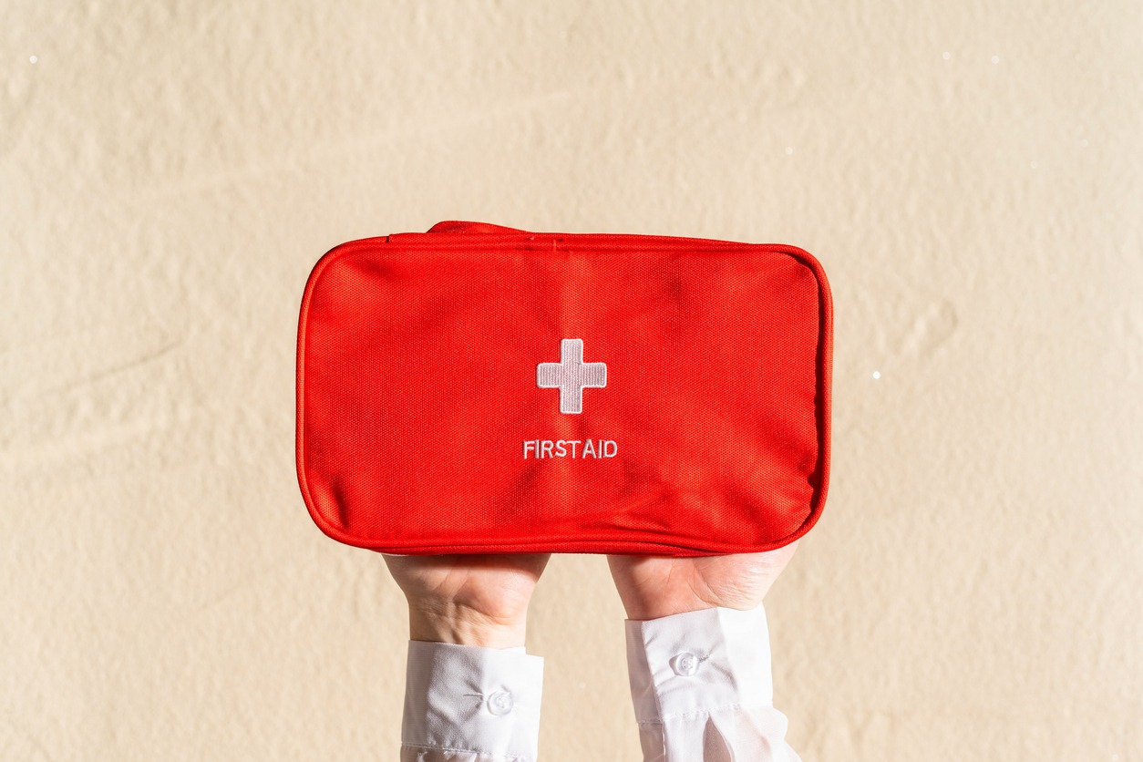On a beach with sand, a woman holding a red first aid bag.