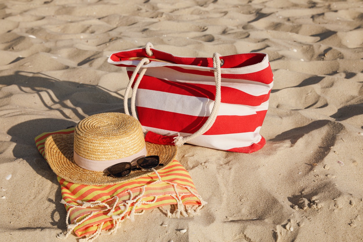 On the sand, a beach bag, a towel, a straw hat, and sunglasses.