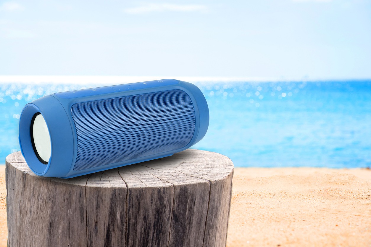 Portable speaker next to sandy beach and stump table.
