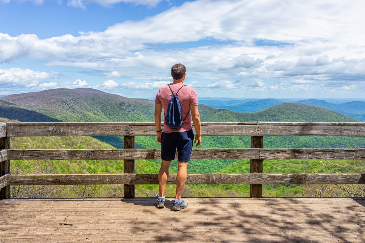 Standing on a wooden platform, a young man carrying a drawstring bag backpack is on the nature Highlands leisure route in Virginia's Wintergreen ski resort town