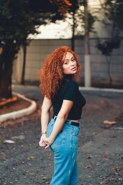 Woman with curly red hair black blouse with blue jeans and black leather