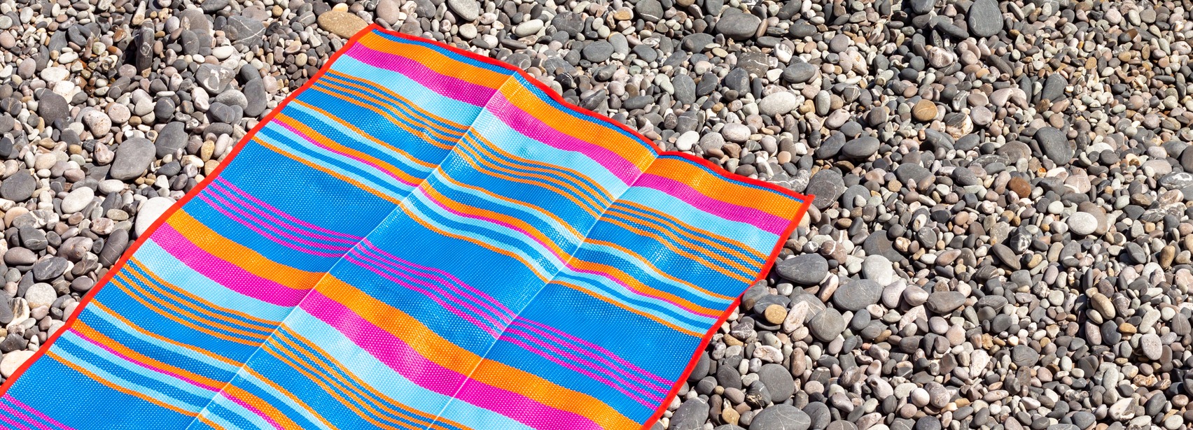a brightly colored beach mat with stripes is placed on a pebbly beach
