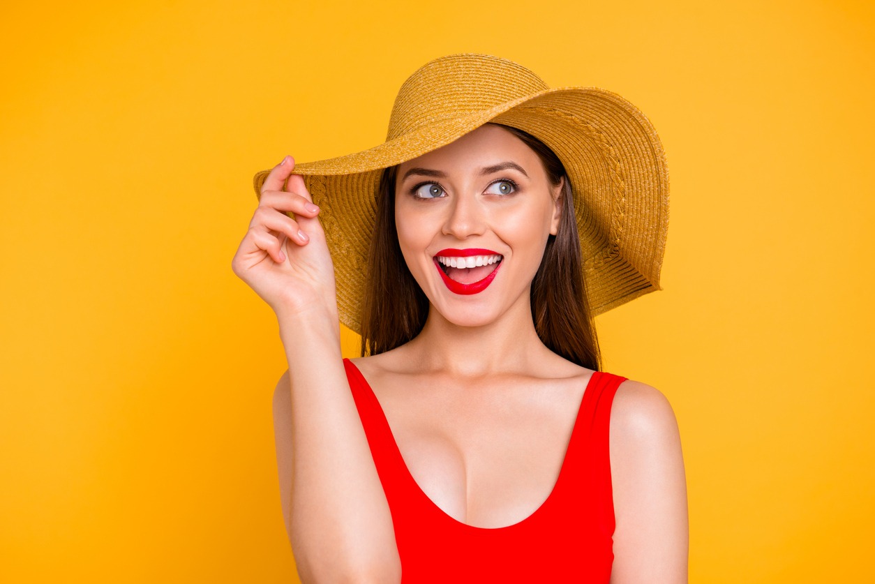 a close up portrait of a girl holding a sun hat with one hand and laughing and looking at the side isolated on a yellow background