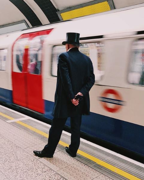 a man in black suit and a top hat, waiting for a train