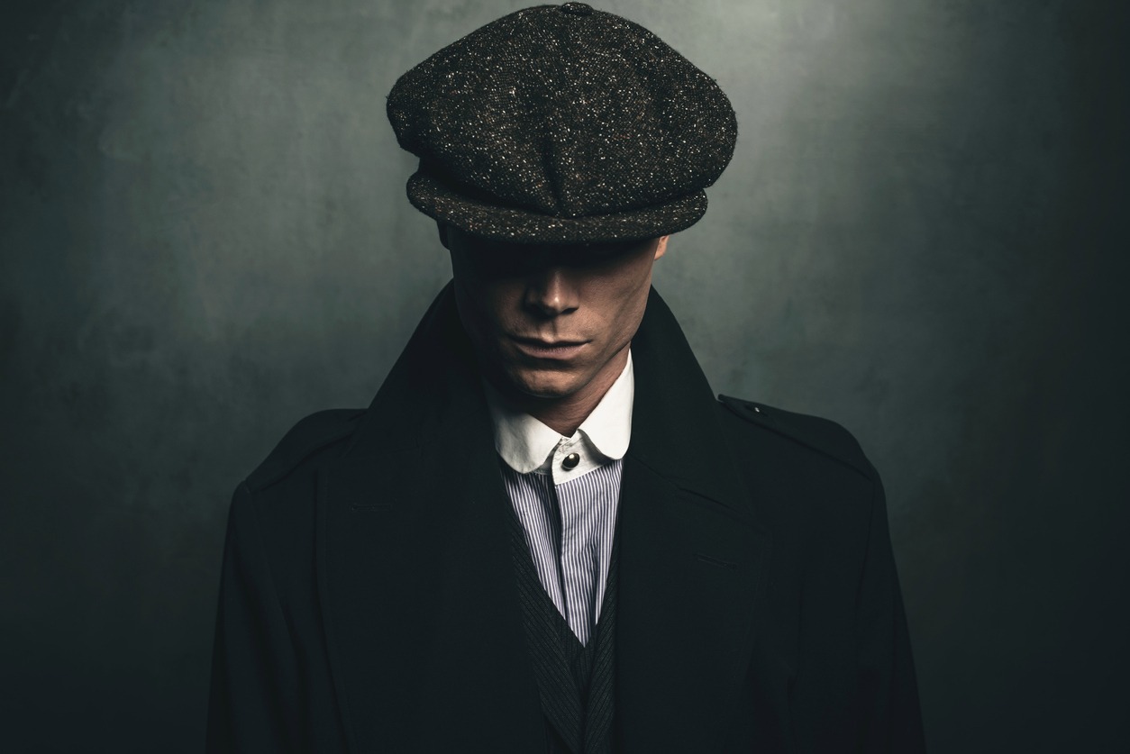 a portrait of retro 1920s english gangster wearing flat cap