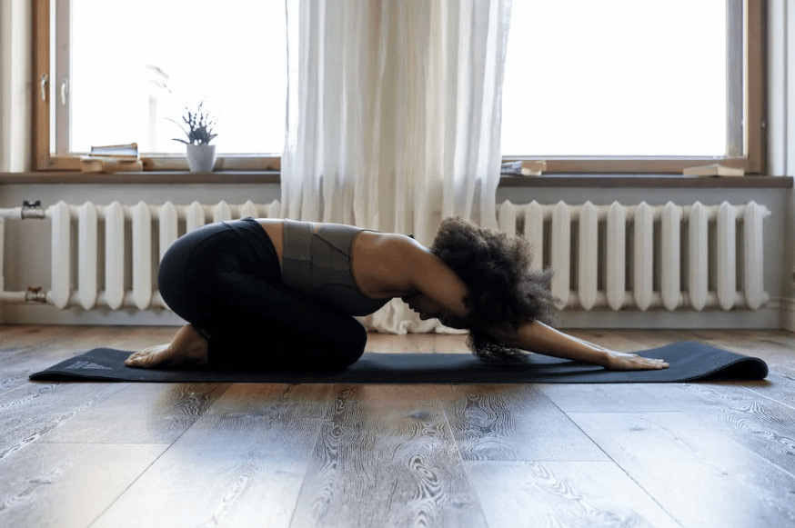 a woman doing a stretch on a black yoga mat