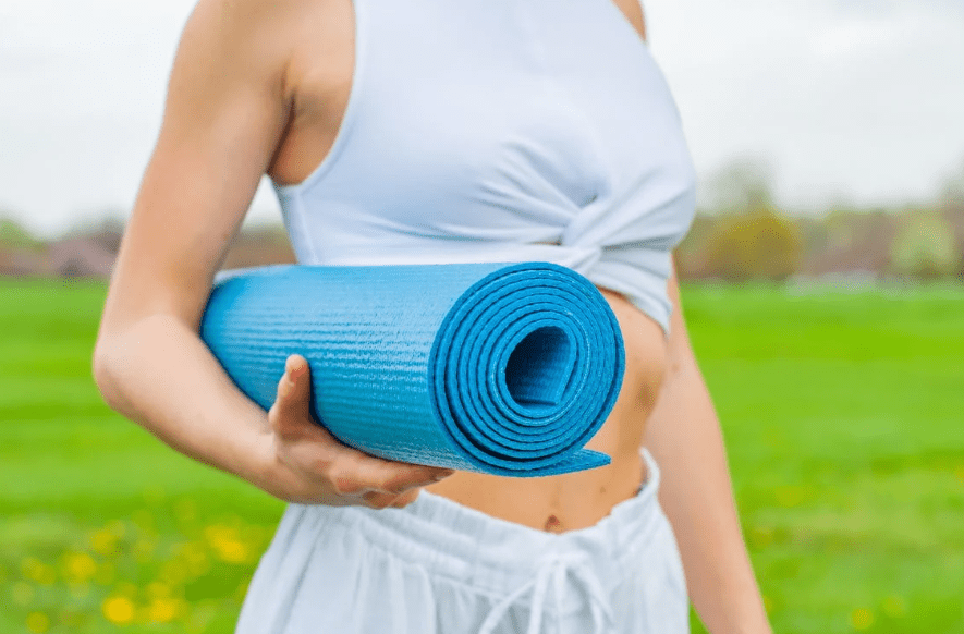a woman standing outdoors carrying a blue yoga mat