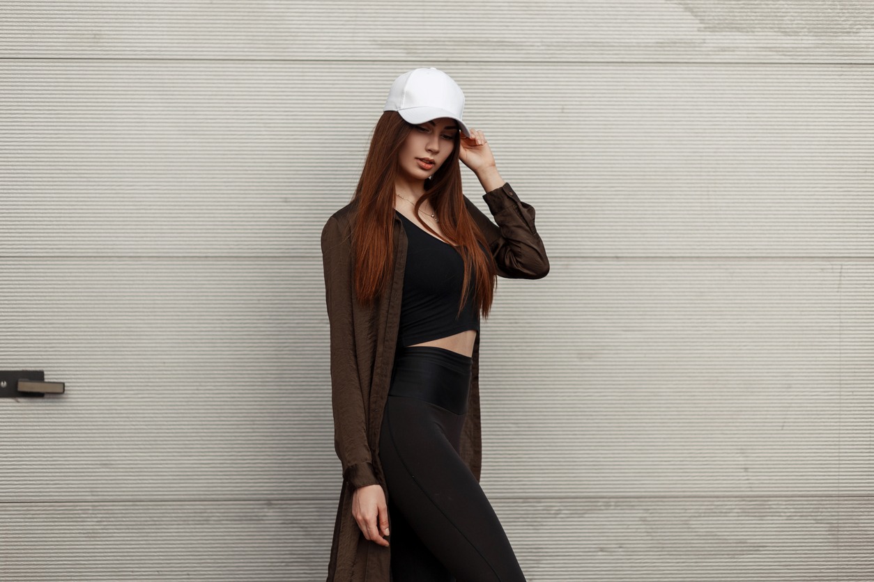 a woman wearing a white cap and fashionable clothes posing near a metal wall