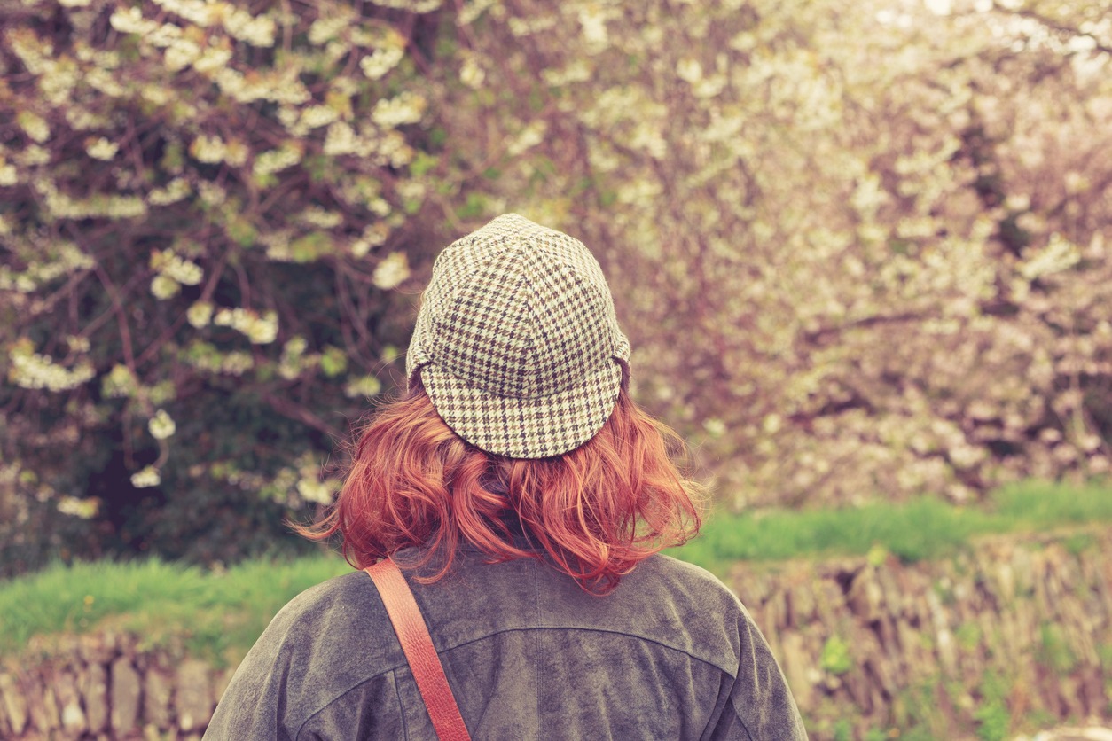 a woman with her back at the camera wearing a deerstalker and looking at trees