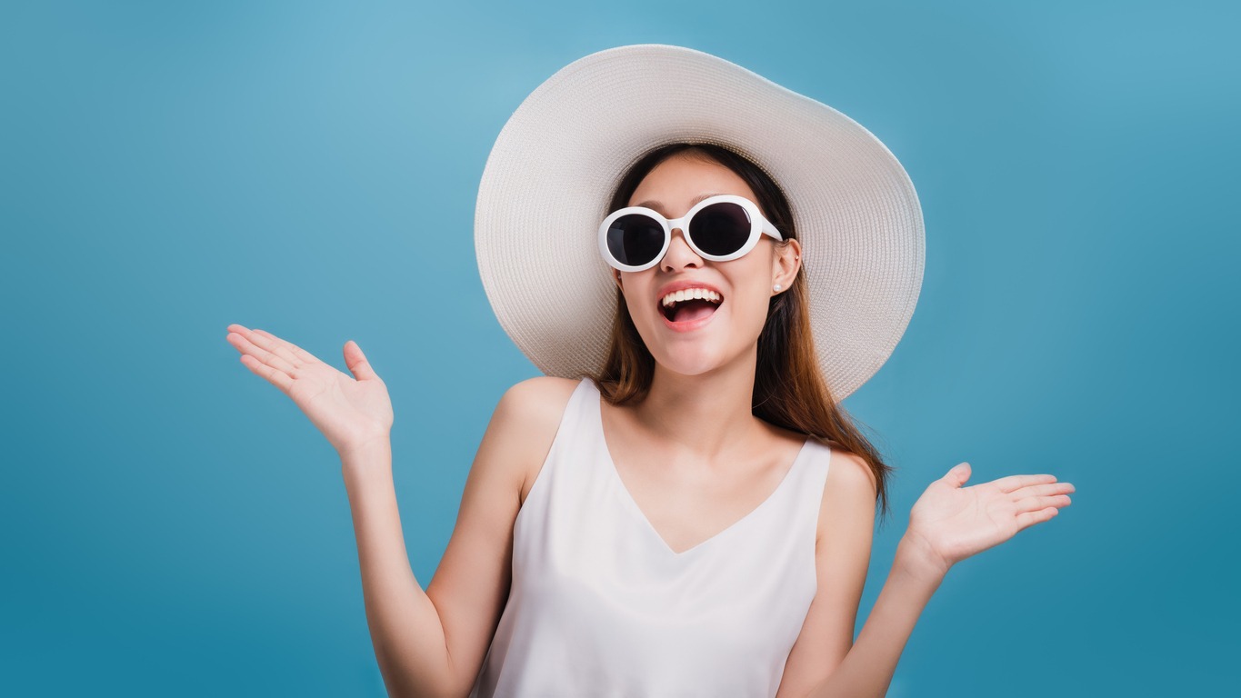 Asian smiling beautiful women blogger wear a wide hat and wear sunglasses isolated in blue color background with copy space.Concept of Travel business with Promotion and Sale