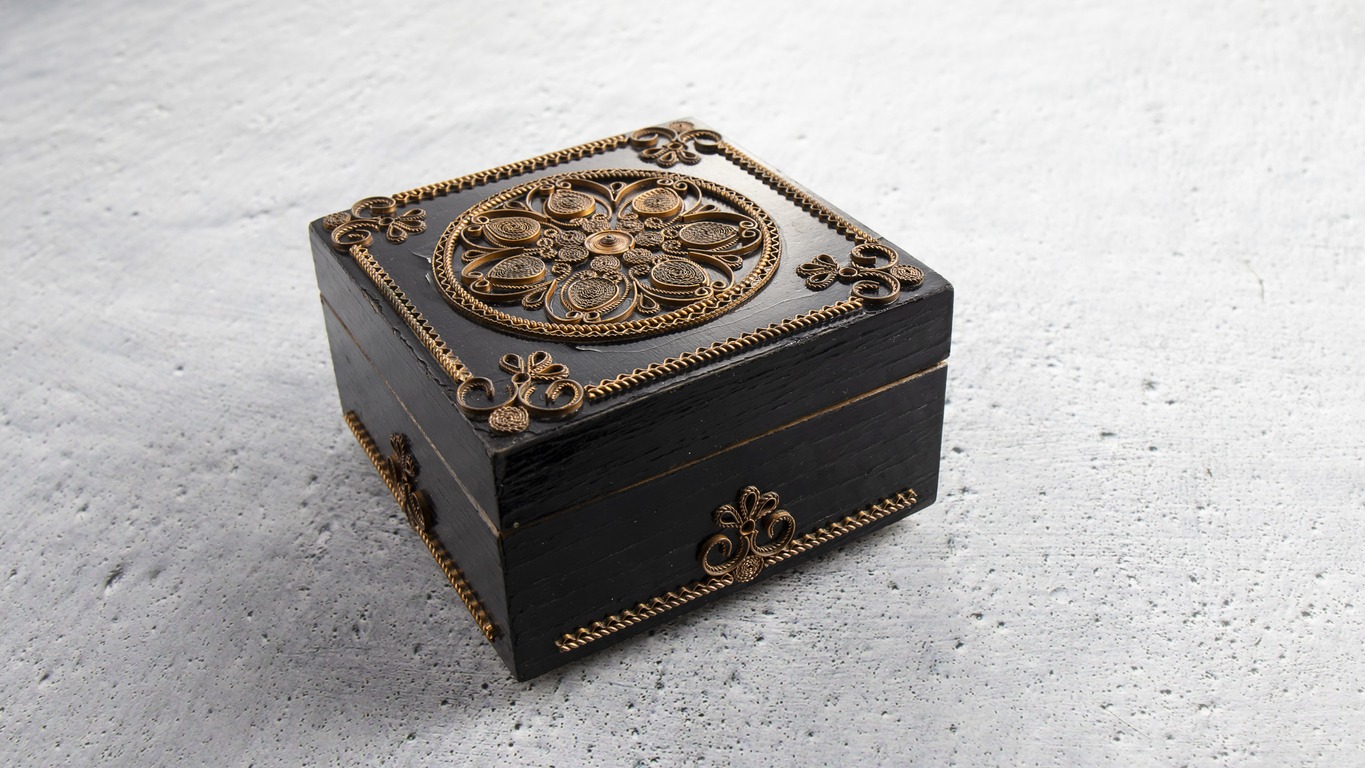 Black vintage wooden jewelry box with ornament on the gray plastered surface.