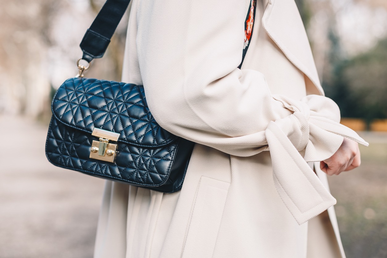 black leather quilted handbag hanging from the shoulder of a woman wearing a beige coat