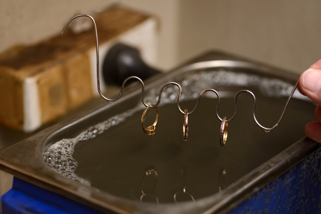 A goldsmith cleans newly polished gold rings in an ultrasonic bath. Sound waves generated in the liquid dislodge particles from the metal