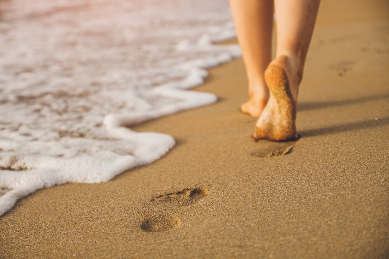 cropped photo of a woman walking on sand on the shore leaving footprints on the sand