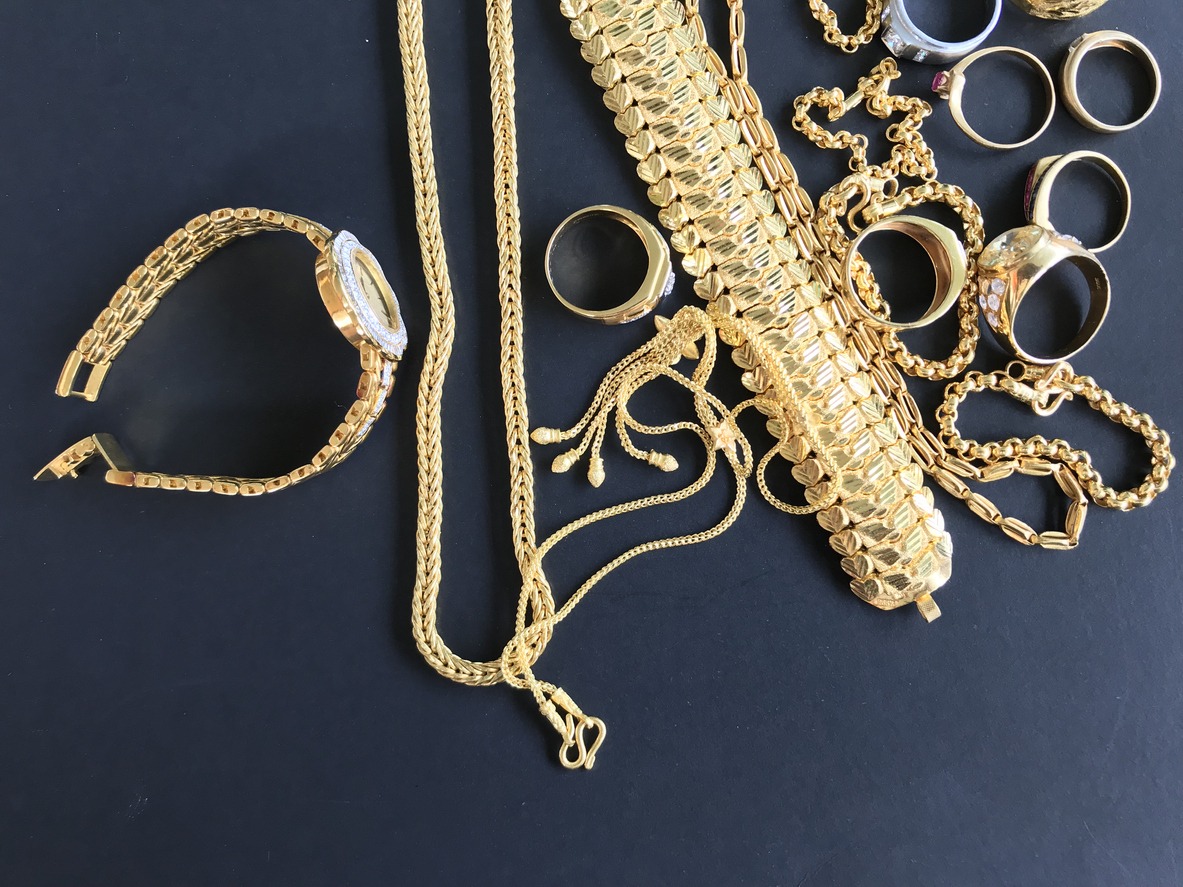 Pile of golden necklace, bracelet, and rings on black background