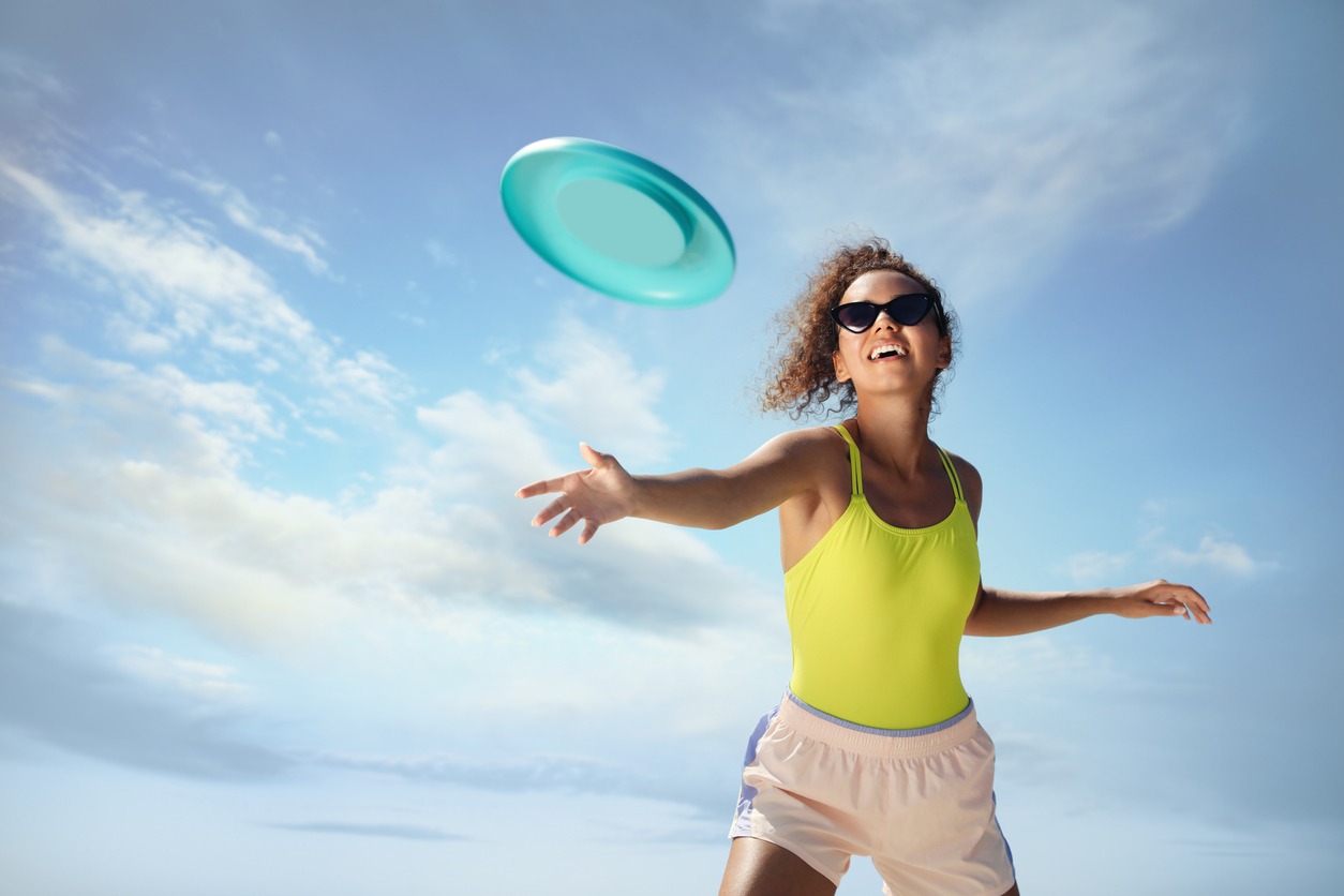 On a sunny day, a joyful African American woman is throwing a flying disk against a blue sky