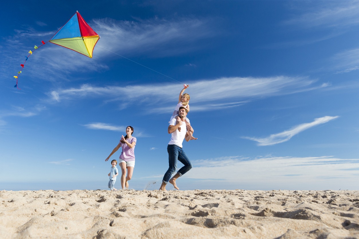 on a beach, a joyful family of four is flying a kite