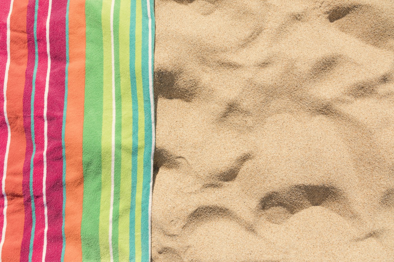 on a sandy, enticing tropical beach, a beach towel with bright stripes is spread out