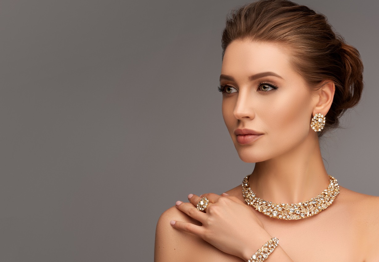 Portrait of alluring woman dressed in a posh jewelry set of necklace, ring and earrings. Pretty model is gazing at the viewer by magnetic look, perfect evening makeup and hair gathered in elegant bun.