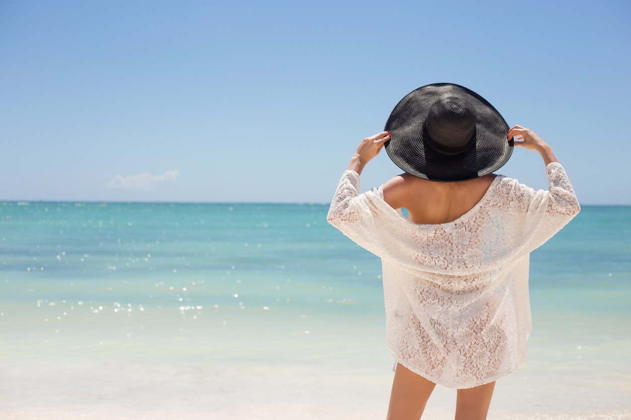Woman in black summer hat on the beach standing with her back to the camera