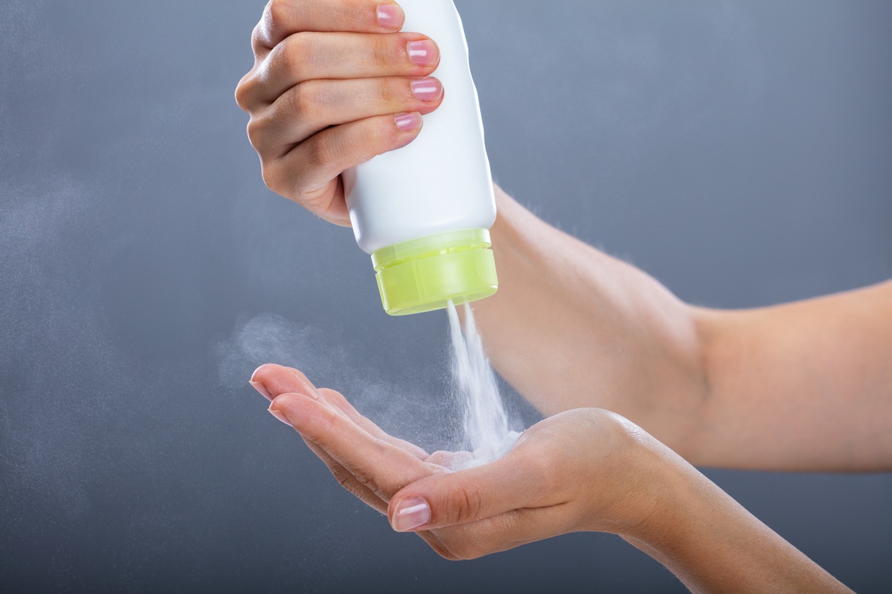 woman's hand is shown dispensing talcum powder from its bottle against a dark background