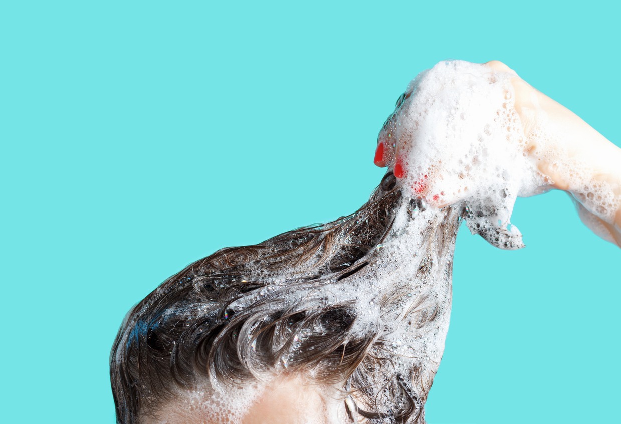 A girl washes her hair with shampoo on a blue background