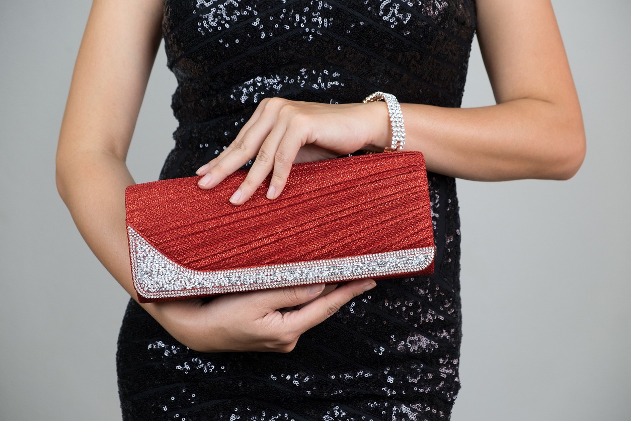A woman in an elegant black dress holding a red and silver clutch bag