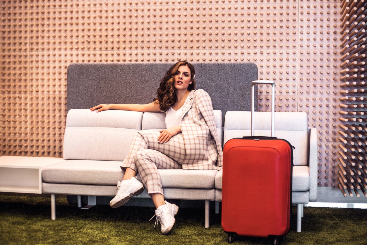 A young, fashionable woman in red luggage is seated in an airport waiting area