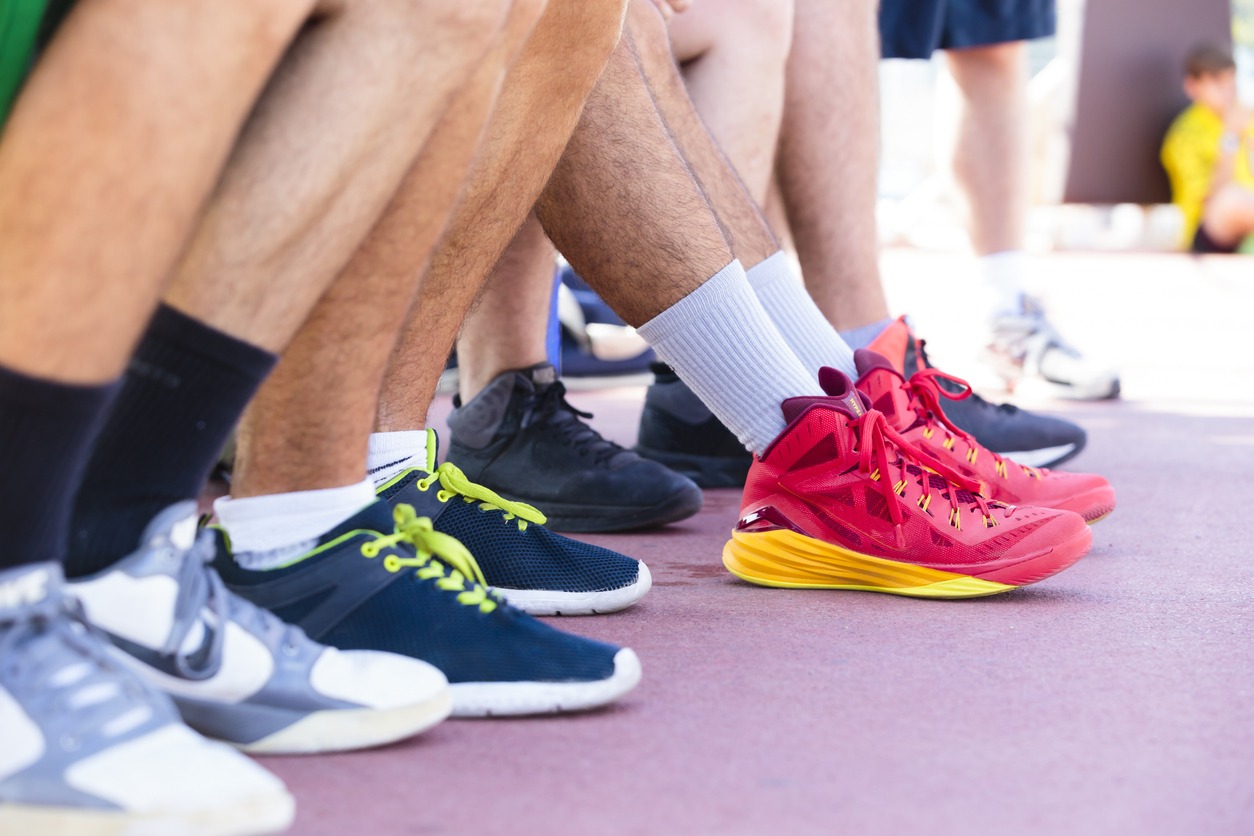 Feet of a team of basketball players sitting on the sidelines waiting to play in assorted sport shoes and trainers, with focus to a young man in a colorful pair of red and yellow footwear
