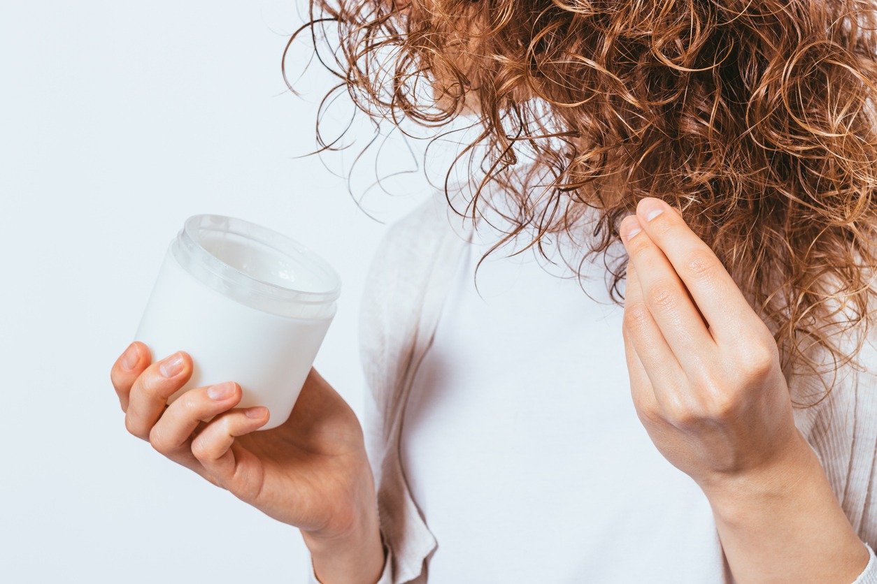 Female's hands apply cosmetic coconut oil on her curly hair tips, close-up