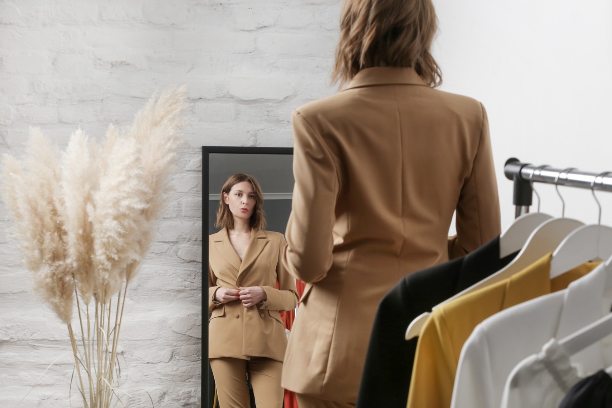 In a boutique or personal wardrobe, a young woman chooses her outfits and tries on a beige blazer