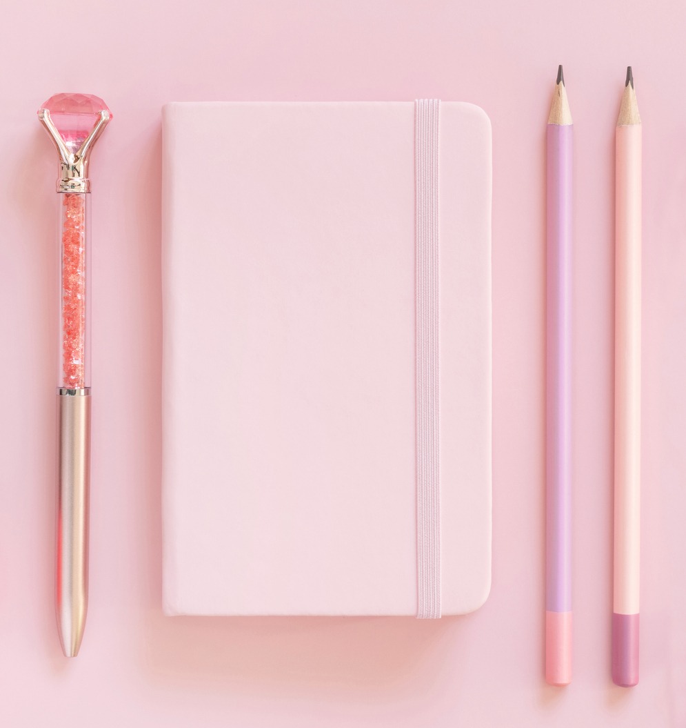Light pink top view with pink notebook, writing tools, and fancy gemstone pen