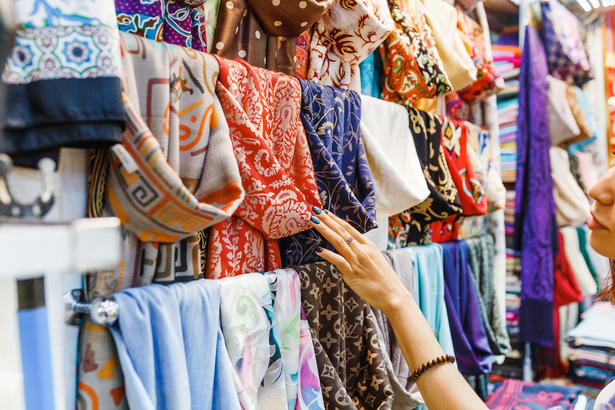 Young woman choosing colorful fabric for her new scarf while shopping in a bazaar