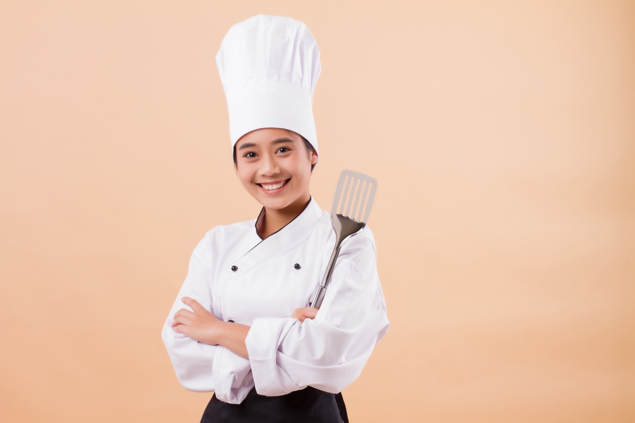 a female chef holding a spatula while wearing her standard uniform