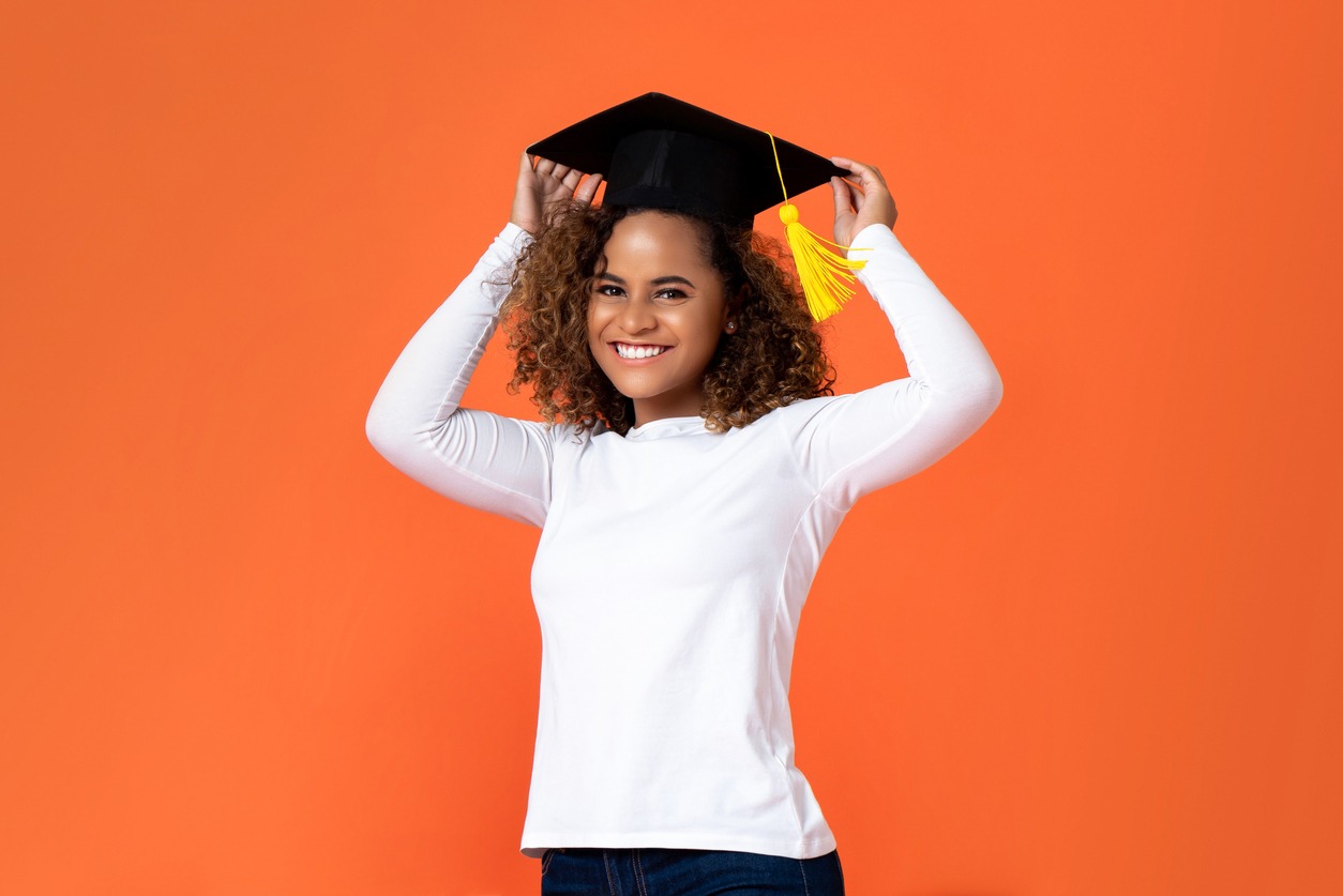 a smiling woman placing a graduation cap on her isolated on an orange background