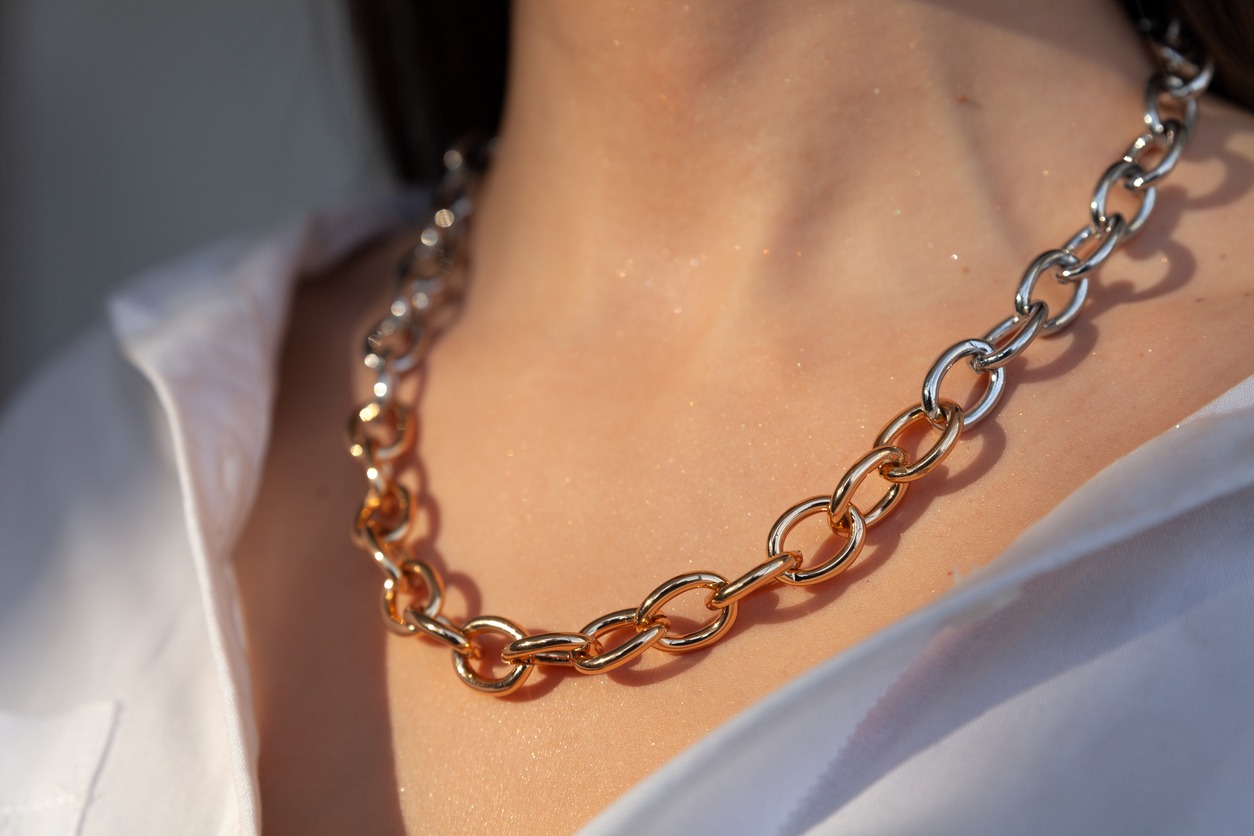 Close-up silver and gold chain on caucasian model brunette with long hair, metal necklace, white shirt neckline, concept modern accessories store, close-up, copy space, horizontal