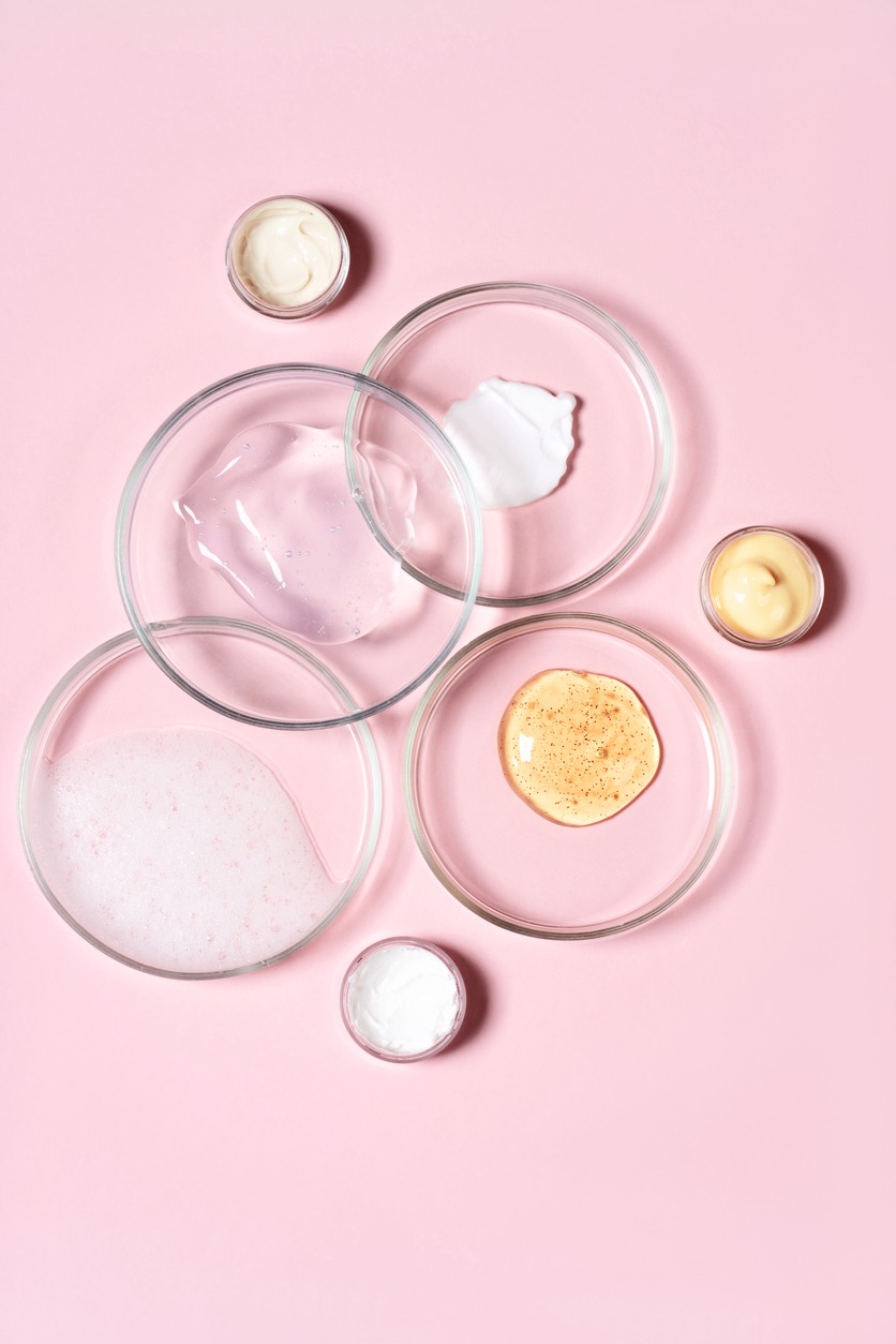Cosmetic products, scrub, face serum and gel in many petri dishes on a pink background. Cosmetics laboratory research concept