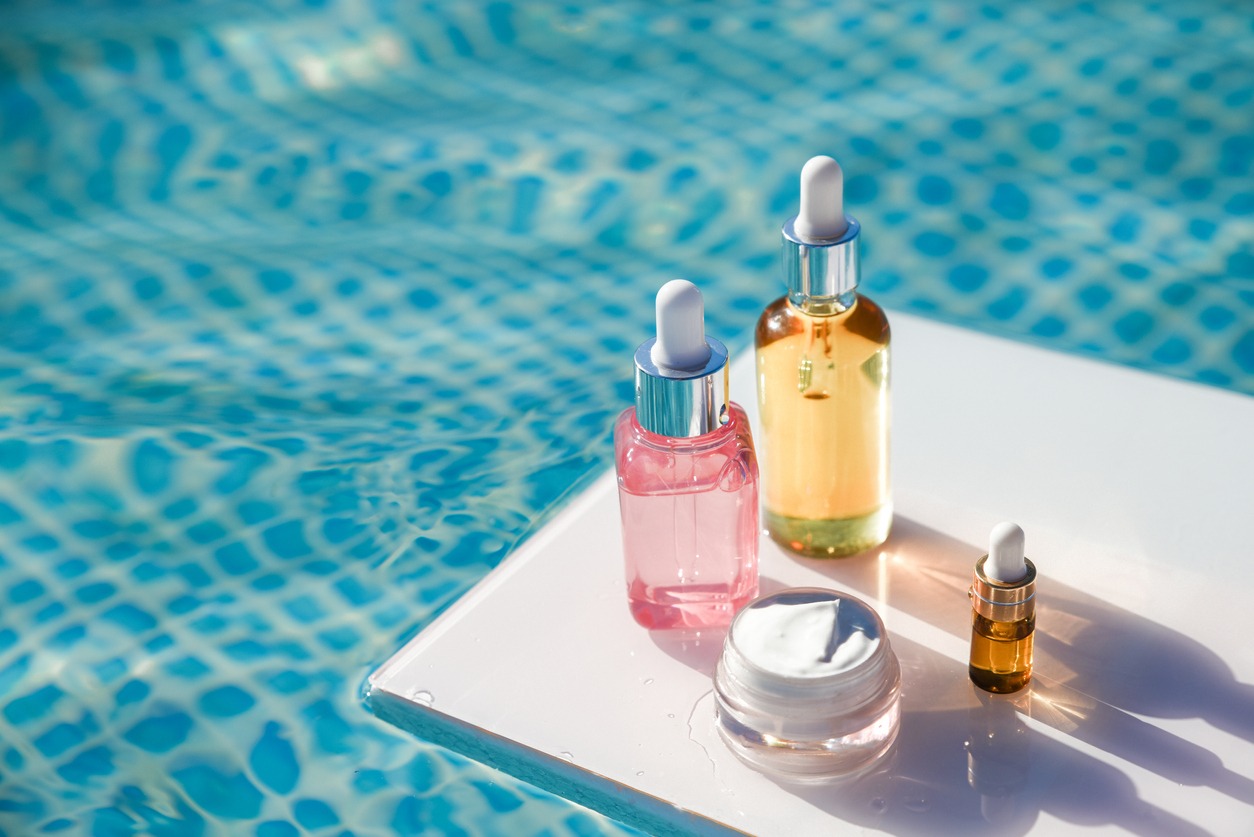 Different packages of cosmetics bottle with serum, sunscreen lotion, sunblock cream on backdrop of water pool on summer day Cream, serum, skin oil body care set Summer sun protection and skin care concept A set of moisturizing and protective SPF cosmetics for travel skin care and tanning