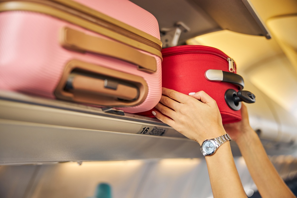 Small piece of luggage being pushed to the top shelf of an airplane by arms.