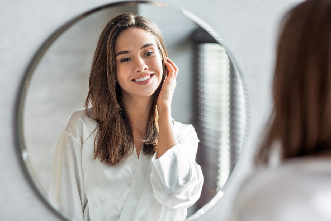 Beauty Concept. Portrait Of Attractive Happy Woman Looking At Mirror In Bathroom