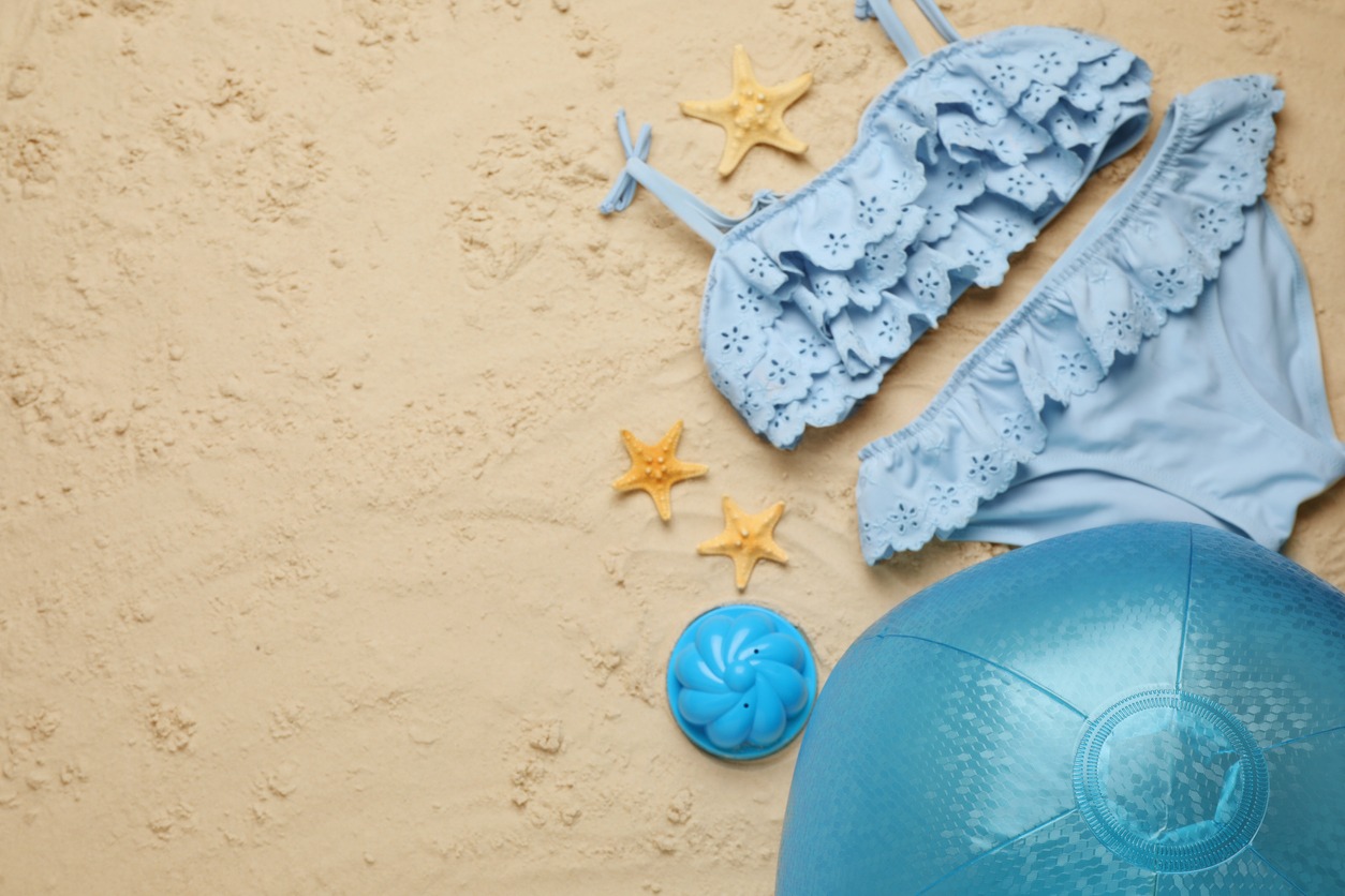 Light blue beach ball, toy, starfishes, and swimsuit on the sand, flat lay. Space for text